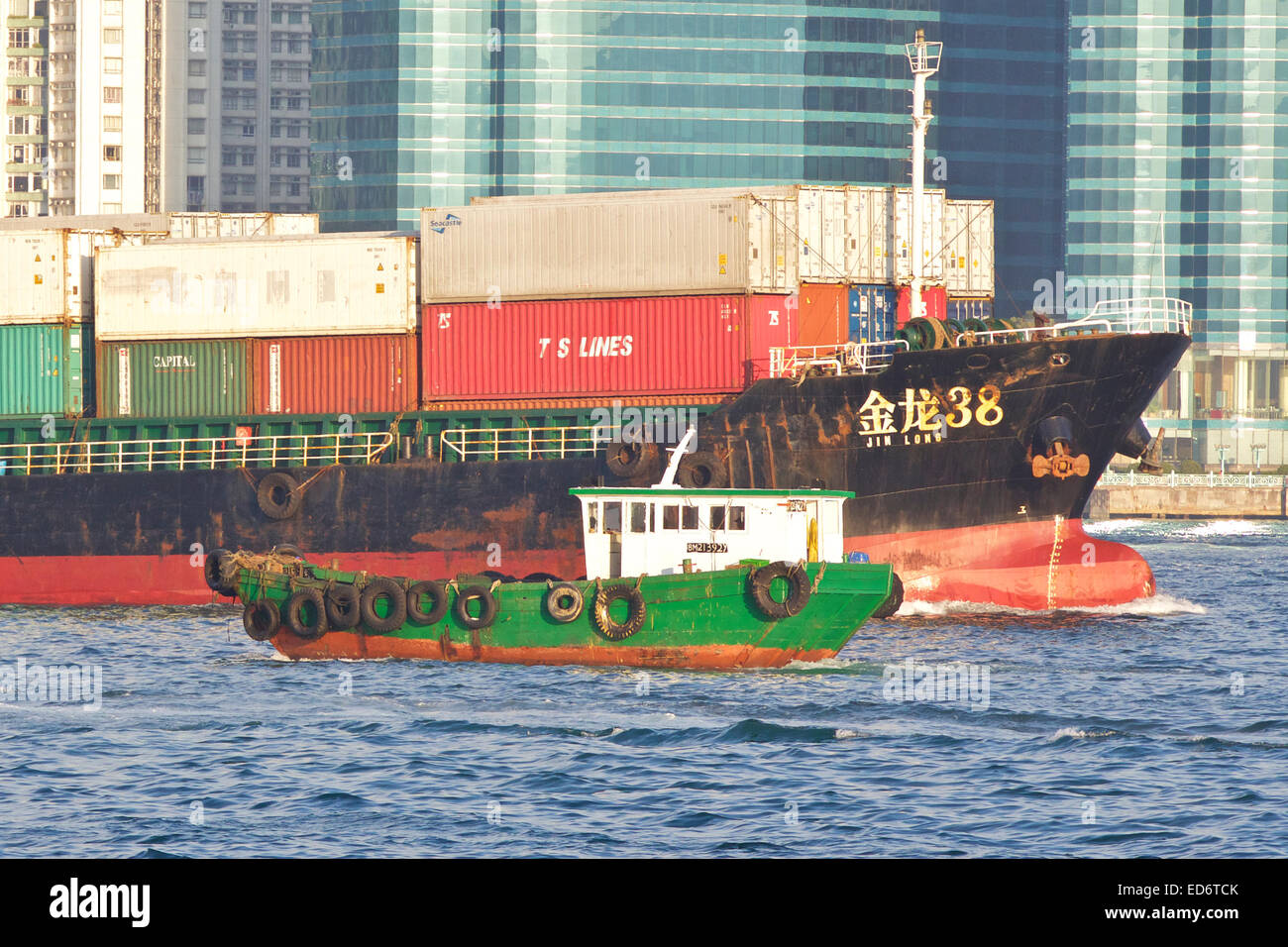 Small Wooden Workboat Passes A Small Container Ship In Kowloon Bay, Hong Kong. Stock Photo
