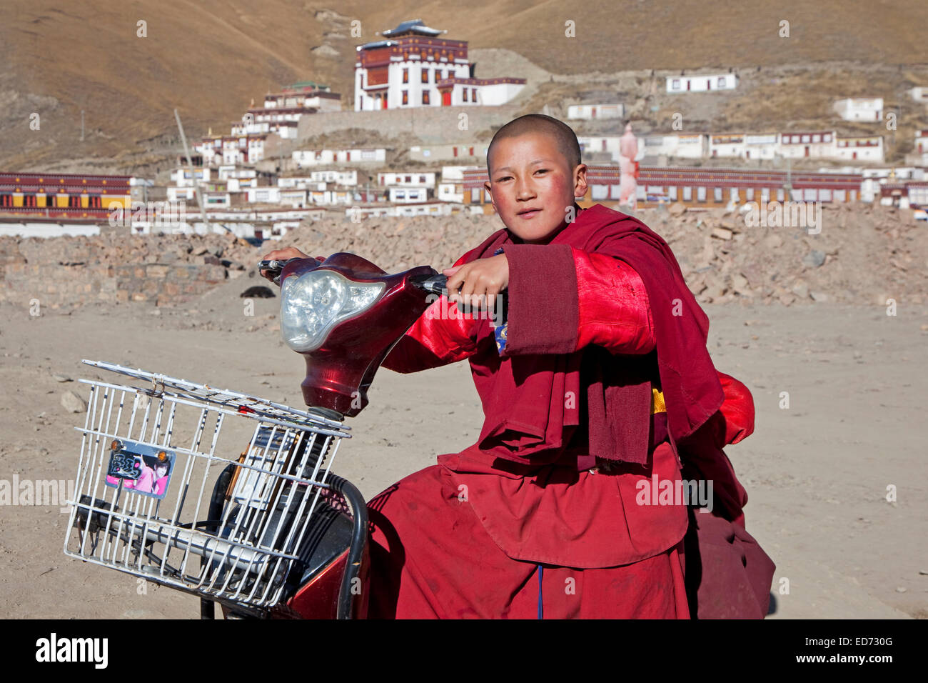 Young monk riding scooter in front of Tibetan monastery Sershu Dzong in the village Sershu / Serxu, Sichuan Province, China Stock Photo