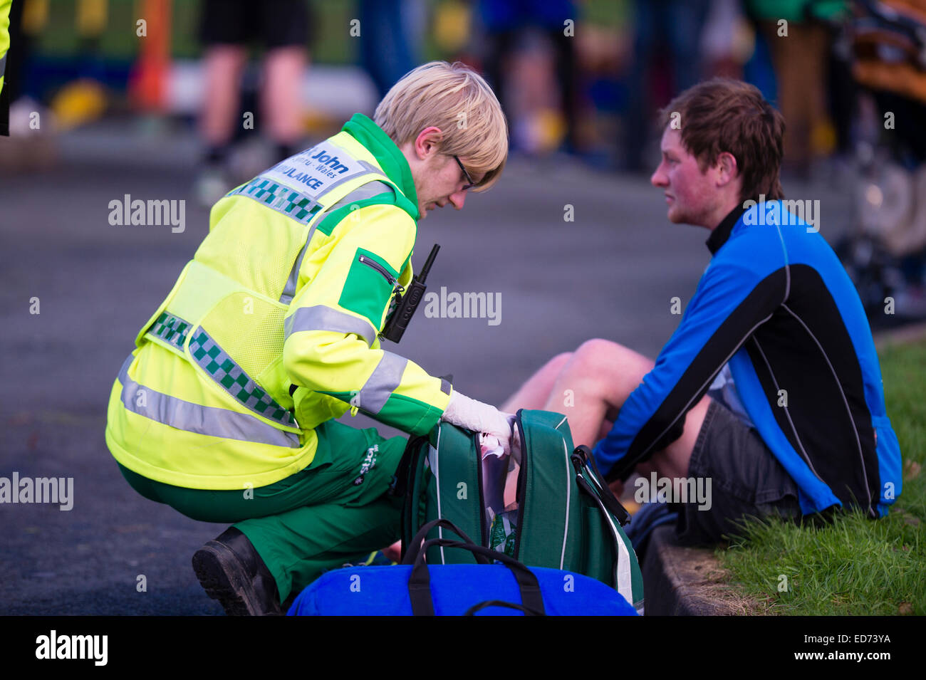 A uniformed  St John Ambulance Wales volunteer first aider  attending to an injured young man person runner at the end of a 10k charity road race, UK Stock Photo