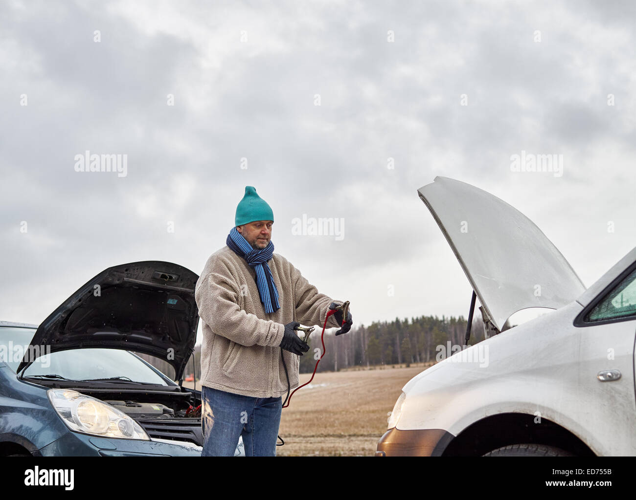 Mid adult man use a jumper cables between the two vehicles Stock Photo