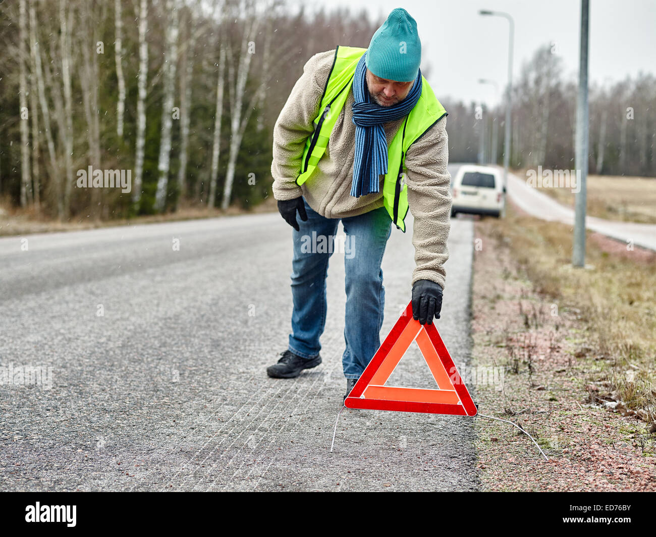 Mid adult man wearing reflector vest and he have a red warning triangle - road and vehicle on background Stock Photo