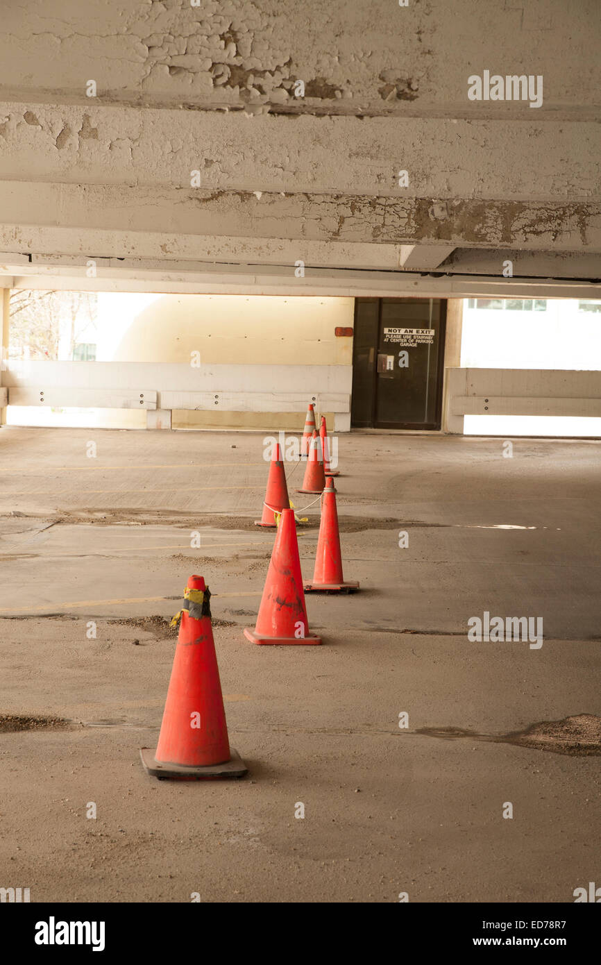 Orange traffic cones direct cars to a safer section of a parking garage in need of repairs. Stock Photo