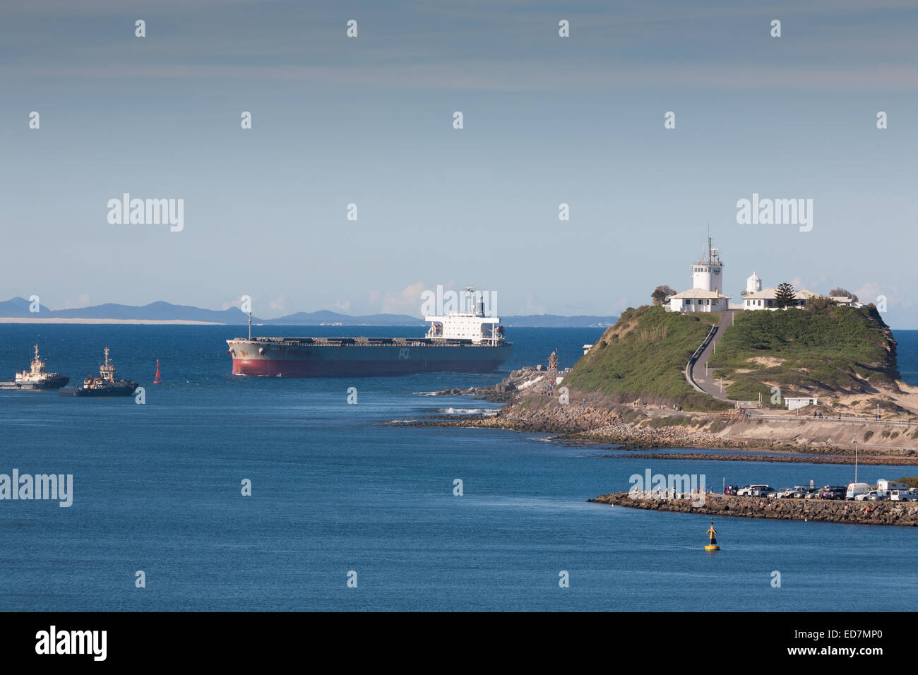 Coal ship passing the Nobbys Head Lighthouse as it approaches its berth in Newcastle NSW Australia Stock Photo