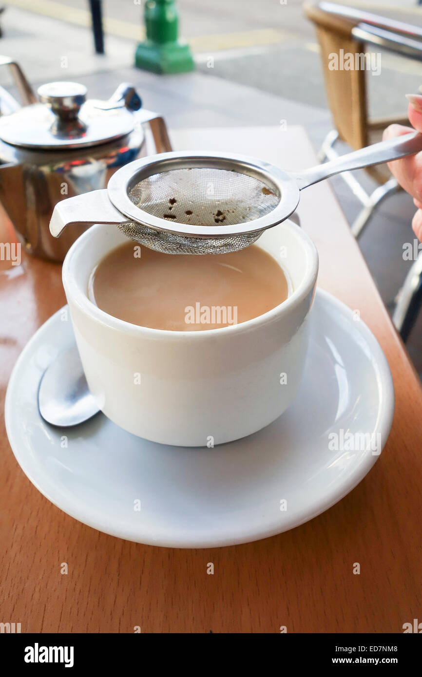Cup of tea being poured using a tea strainer Stock Photo Alamy