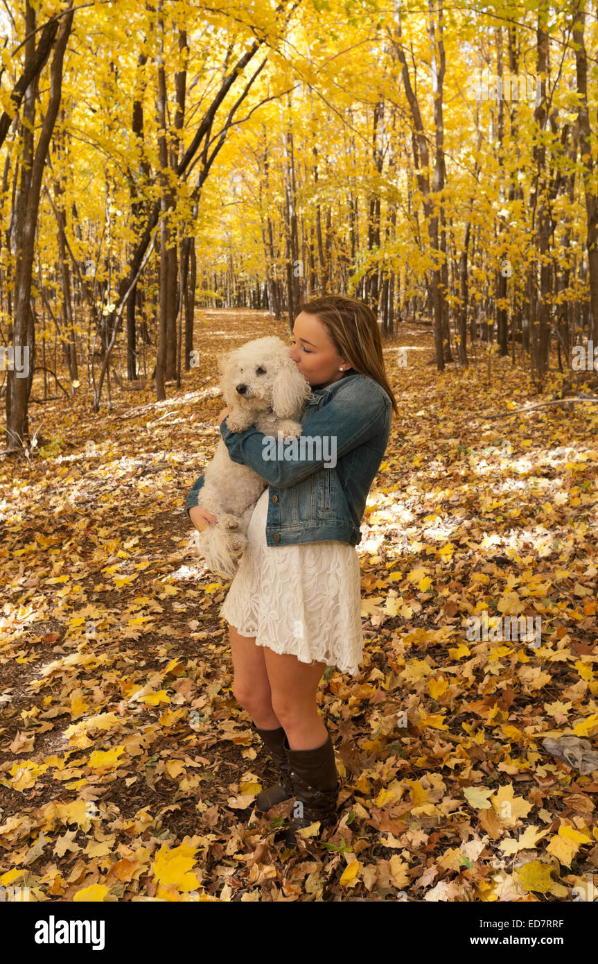 full length portrait of young female teen on forest trail kissing dog in autumn Stock Photo