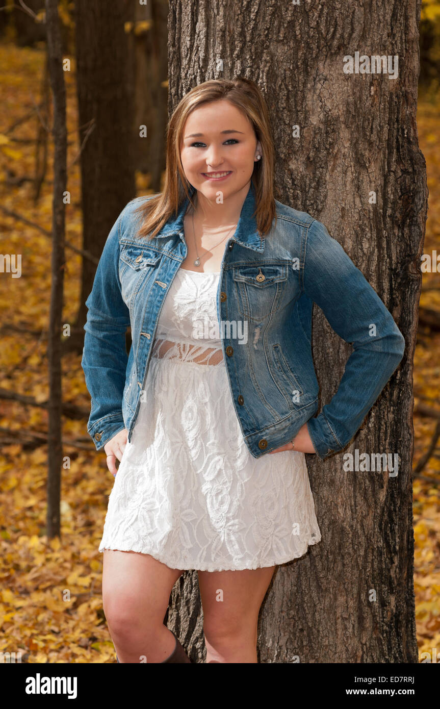three quarter length portrait of young female teen smiling and standing against tree in autumn forest Stock Photo