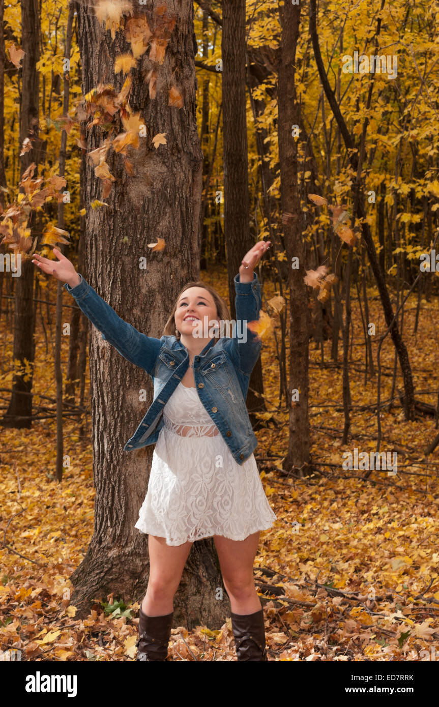 young female teen in forest having fun smiling and tossing leaves in autumn Stock Photo
