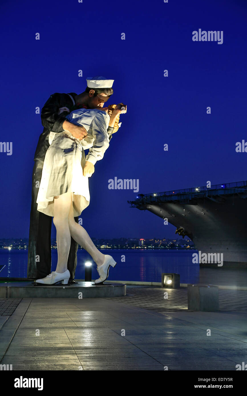 "Unconditional Surrender" sculpture (sailor kissing nurse), by Seward Johnson, and USS Midway aircraft carrier, San Diego Calif Stock Photo