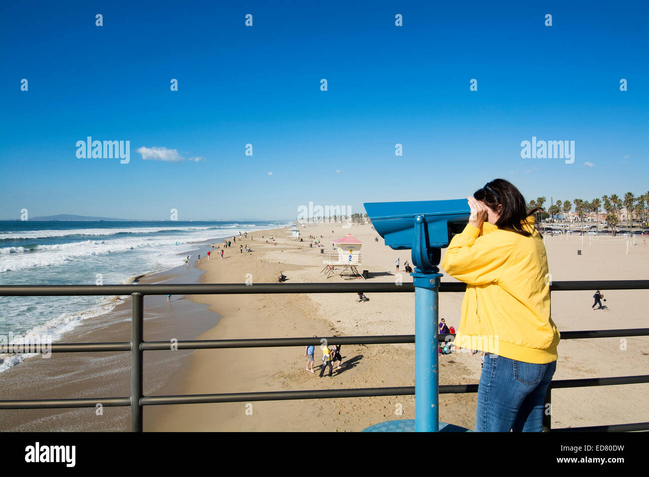A tourist on the Huntington Beach pier watches surfers through coin operated binoculars during a bright, sunny day. T Stock Photo
