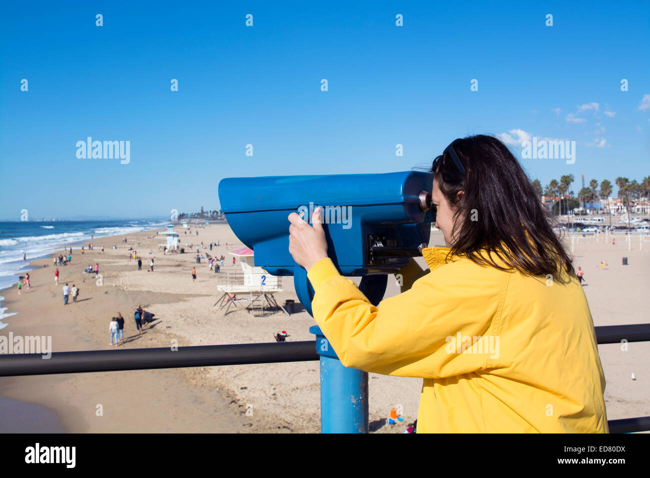 A tourist on the Huntington Beach pier watches surfers through coin operated binoculars during a bright, sunny day. Stock Photo