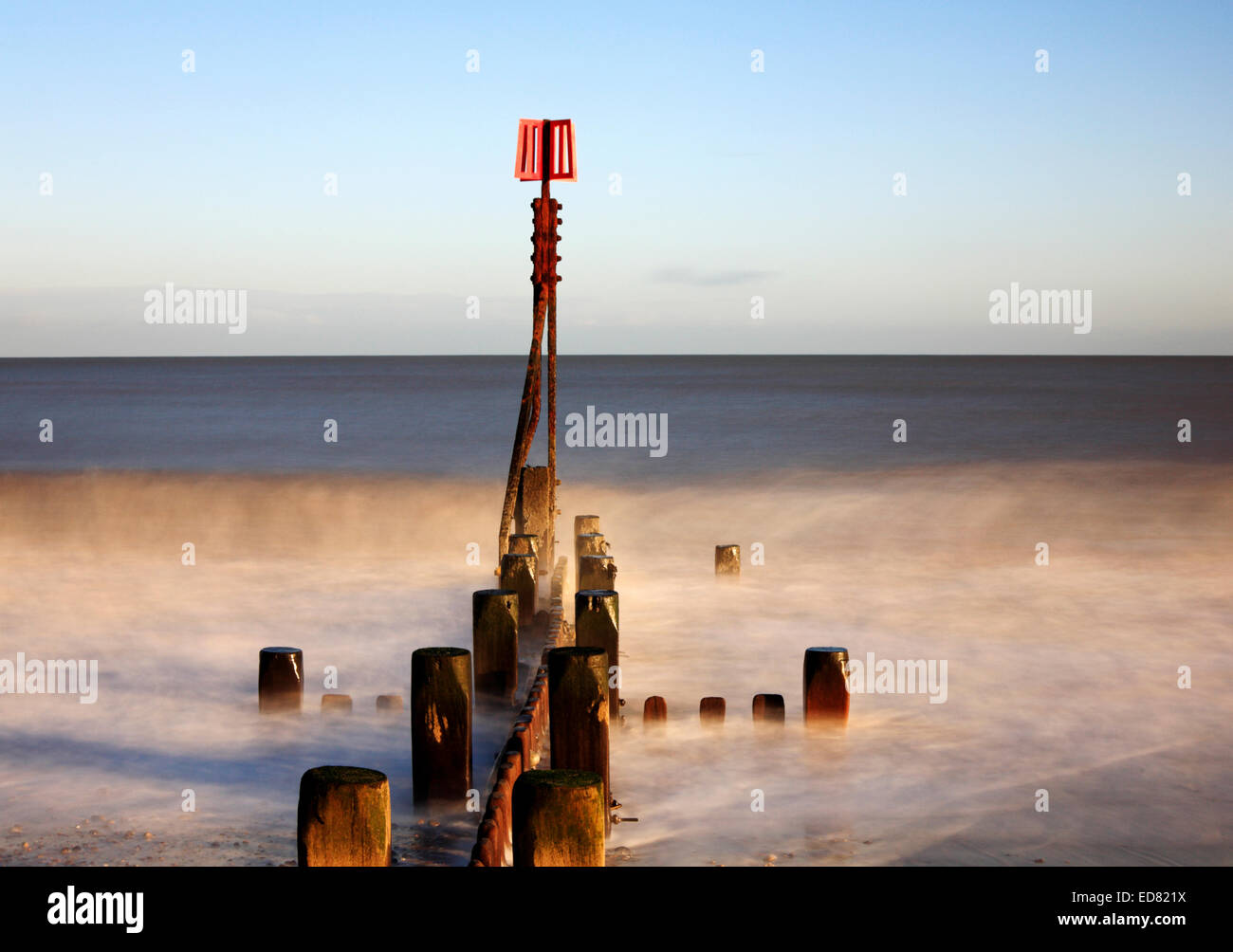 A creative image of a breakwater with marker post in a moderate sea at Cart Gap, Norfolk, England, United Kingdom. Stock Photo