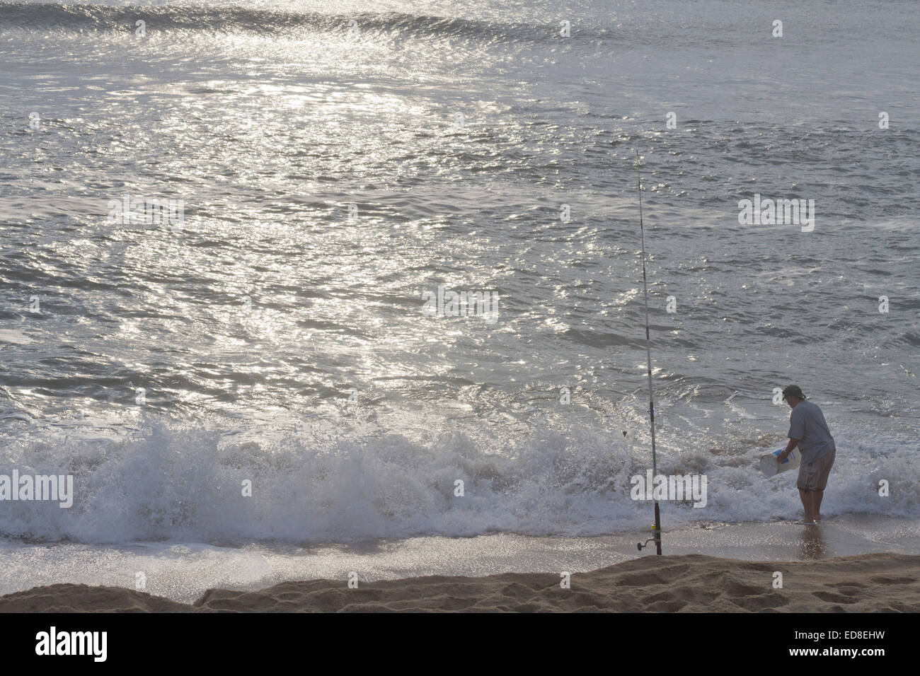 Cape Hatteras, Outer Banks, North Carolina, USA - October 18, 2013:  Man washes a bucket in the sea next to his fishing pole Stock Photo