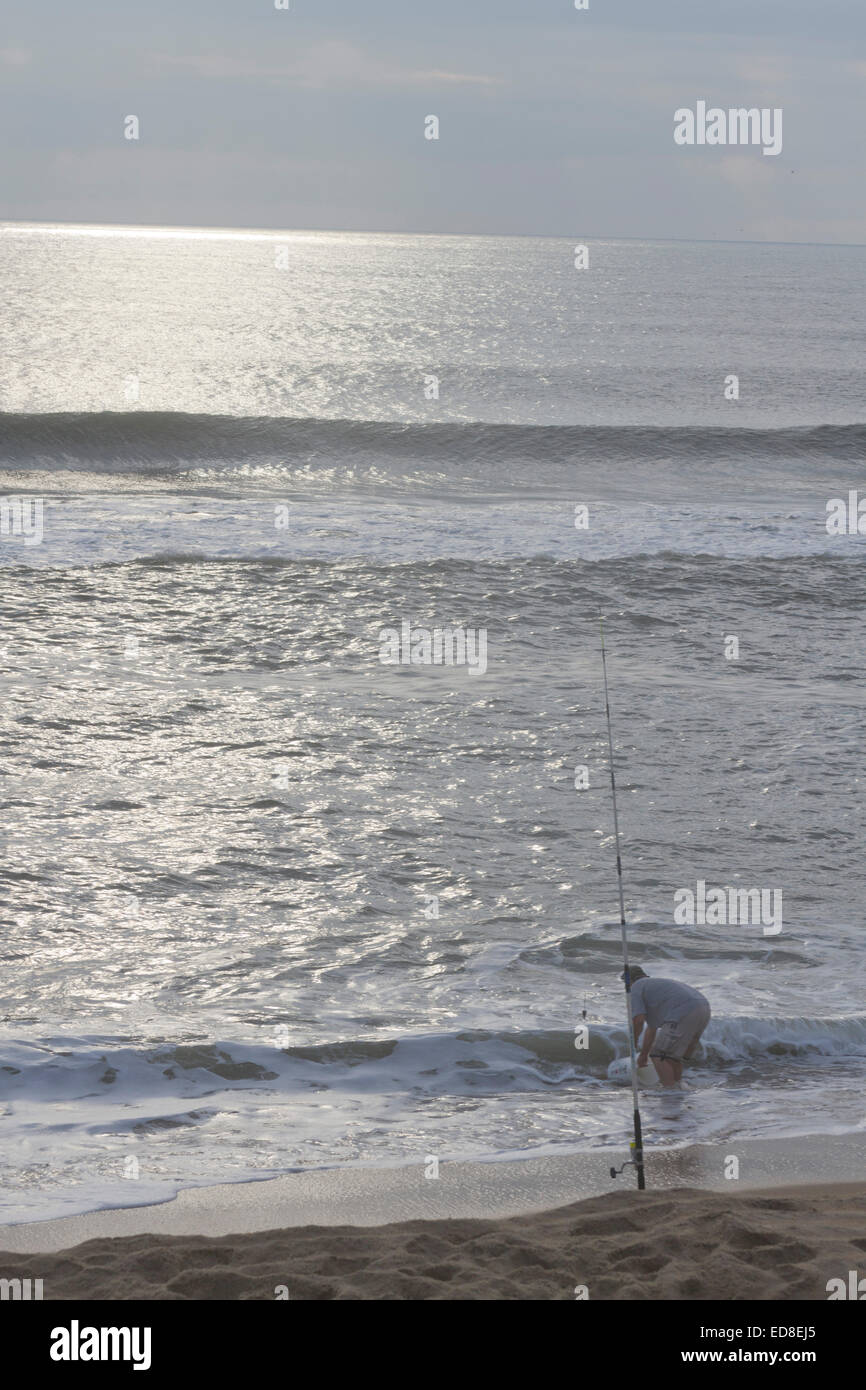 Cape Hatteras, North Carolina, USA - October 18, 2013:  Man bends over to wash a bucket in the sea next to his fishing pole Stock Photo