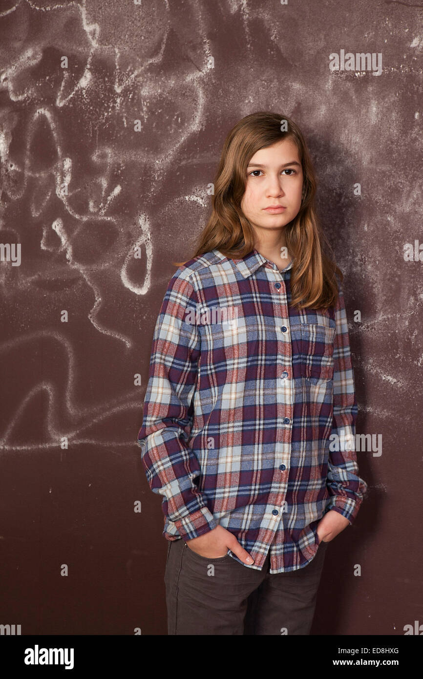 sad teenager girl in chequered shirt and jeans standing near brown wall Stock Photo