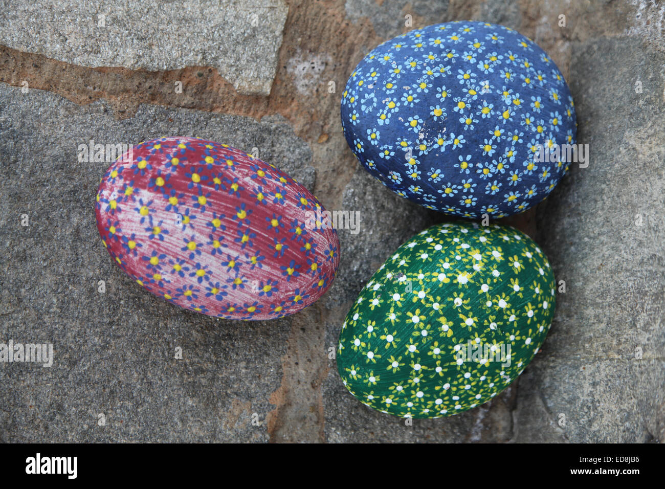Three brightly coloured stones painted in a striking 'aboriginal' style, red, blue and green with flower motives overall. Stock Photo