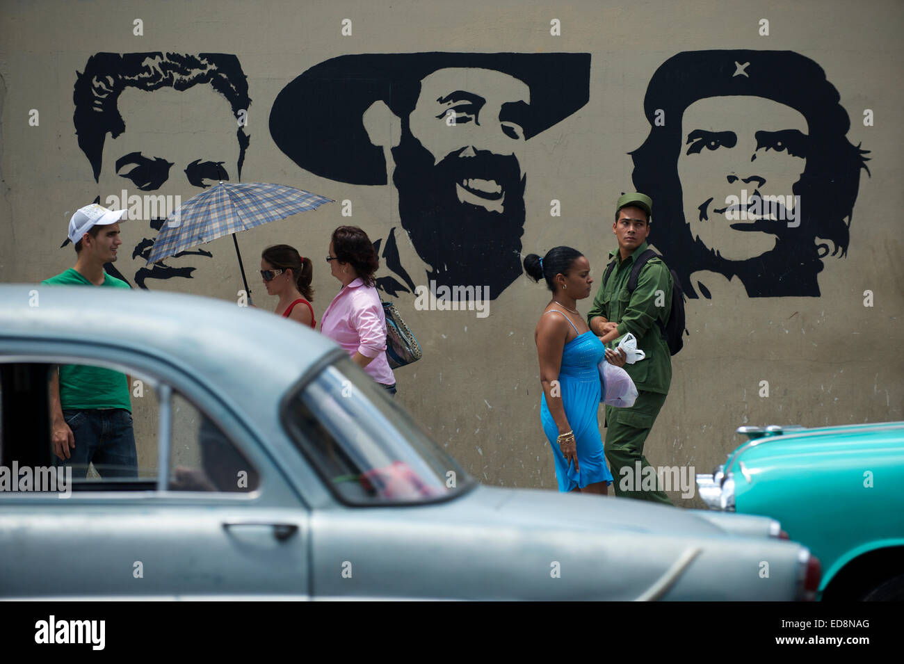 HAVANA, CUBA - JUNE, 2011: Pedestrians and classic American cars pass in front of stencil billboard of Communist heroes. Stock Photo