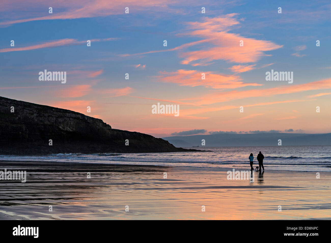 Couple walking dog on beach at sunset, Southerndown, Wales, UK Stock Photo