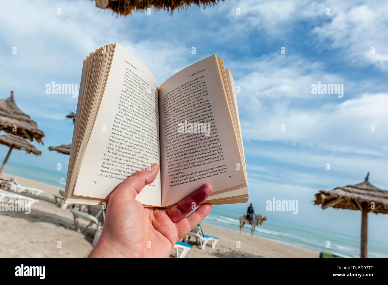 Reading a paperback book on a sun lounger on the beach at Djerba ...