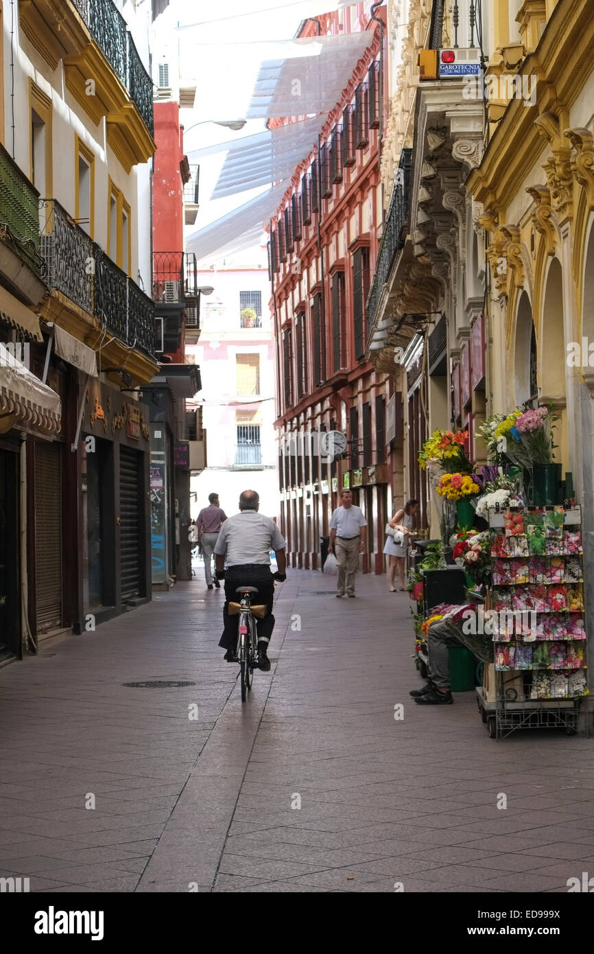Seville Spain: Man cycling along narrow shopping street in Seville Spain Stock Photo