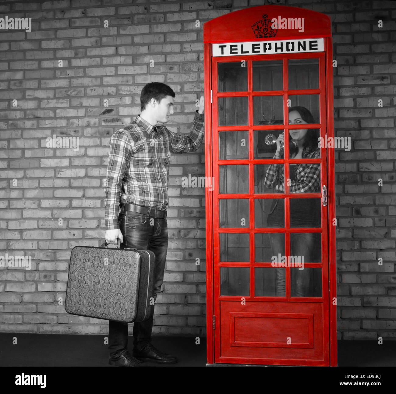 Young Handsome Man Holding Suitcase Knocking at the Telephone Booth with Woman Talking Inside. Captured with Gray Scale Effect. Stock Photo