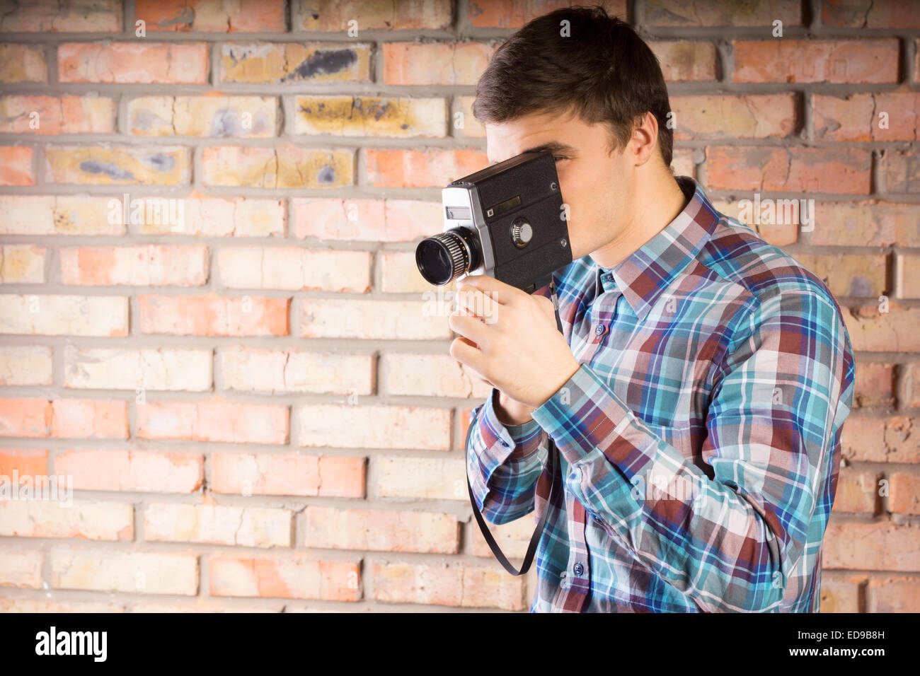 Young Handsome Man in Long Sleeve Shirt Taking Picture Using Vintage Camera with Brick Wall Background. Stock Photo