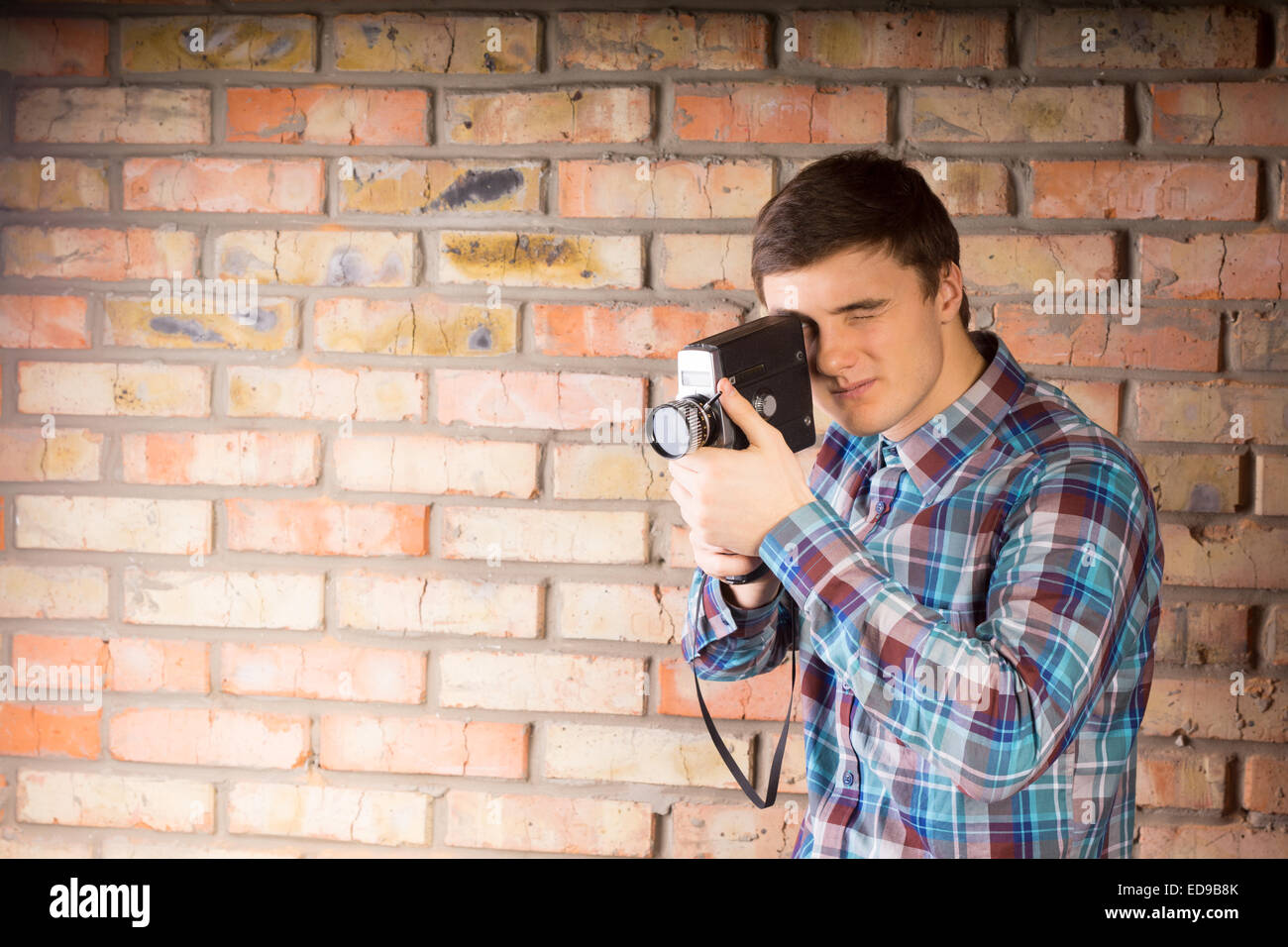 Handsome Young Photographer in Casual Long Sleeve Shirt Capturing Something Using Camera on Brick Wall Background. Stock Photo