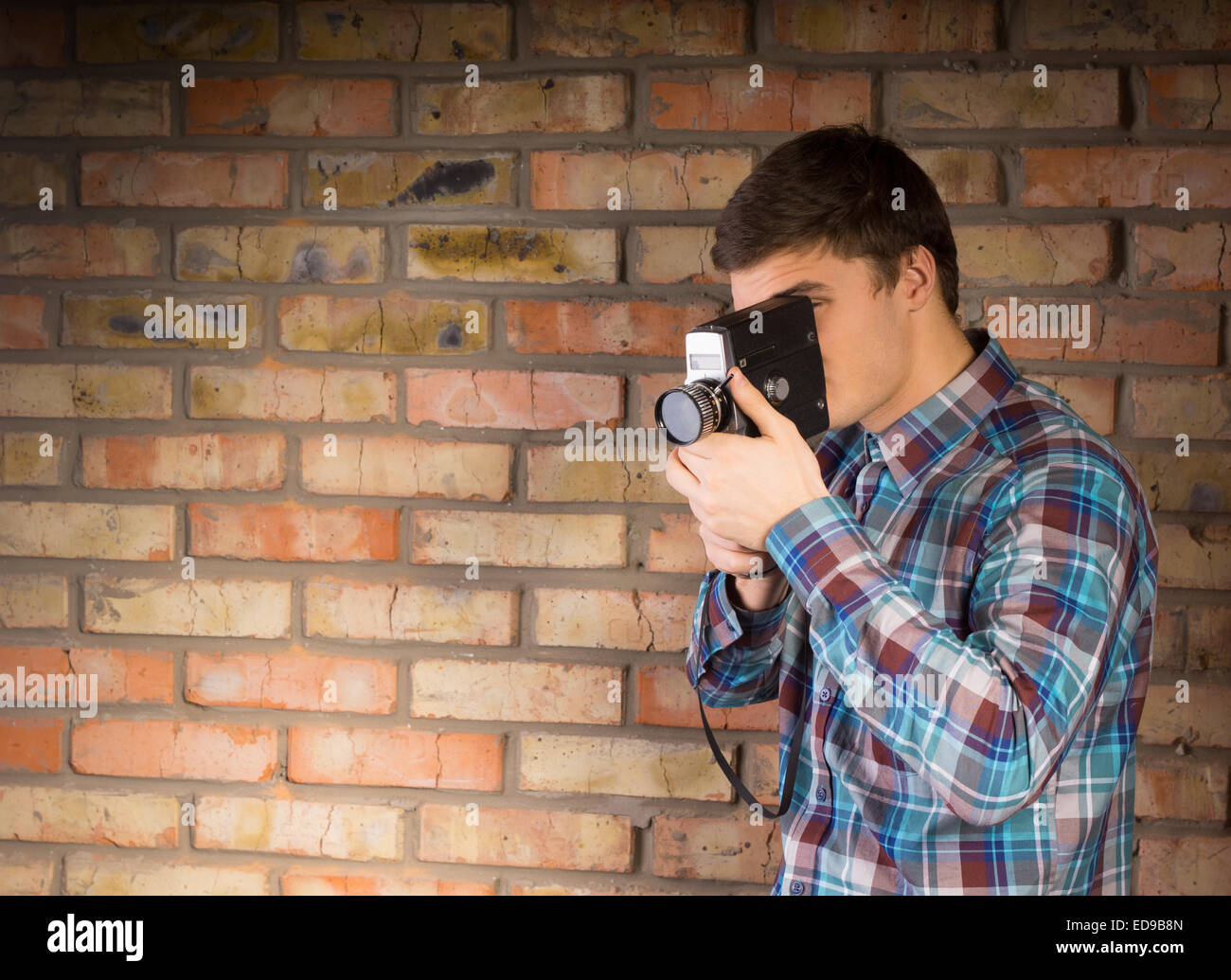 Close up Young Man in Checkered Long Sleeve Shirt Recording Something Using Portable Device on a Brick Wall Background. Stock Photo