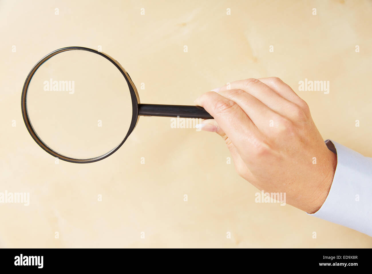 Female wand holding a magnifying glass over table Stock Photo