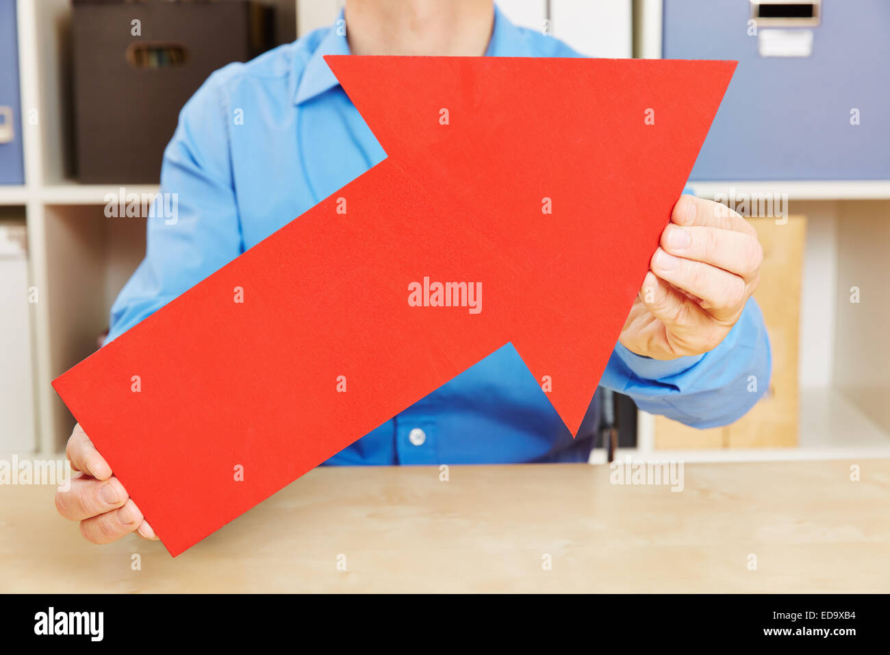 Man holding big red arrow pointing up in his office Stock Photo - Alamy