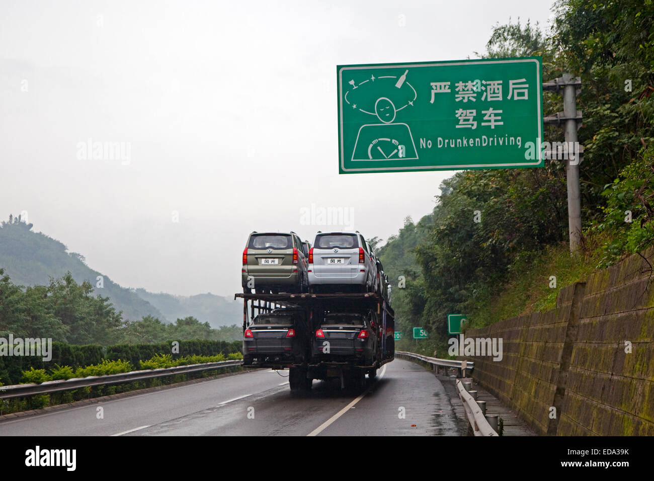 Typical Chinese side-by-side double-decker car transporter and No Drunken Driving roadsign along highway, Yunnan Province, China Stock Photo