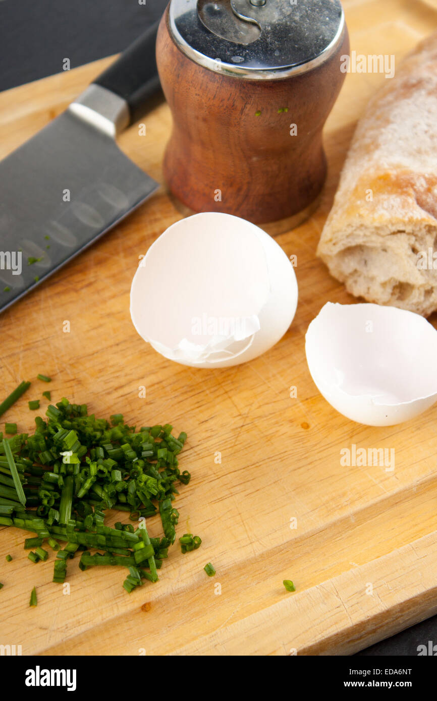 Egg shell, bread, knife, chives and pepper mill neatly arranged on cutting board. Stock Photo