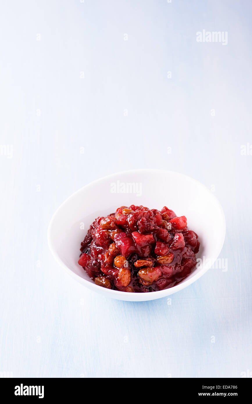 Pear cranberry relish in a white bowl over light blue background with ...