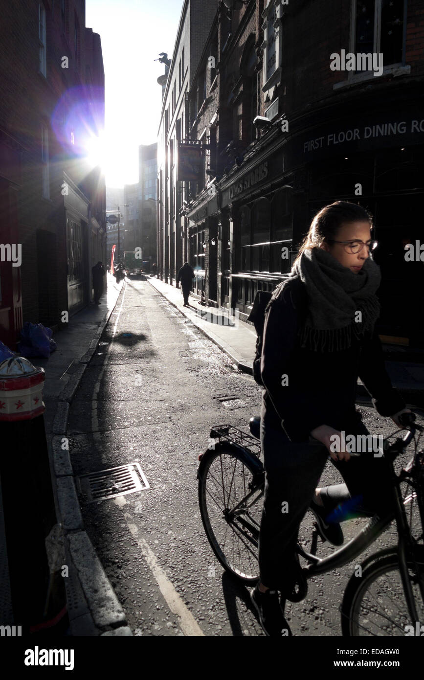 A young woman cycles along Sandy's Row on a sunny winter morning in Spitalfields East London KATHY DEWITT Stock Photo