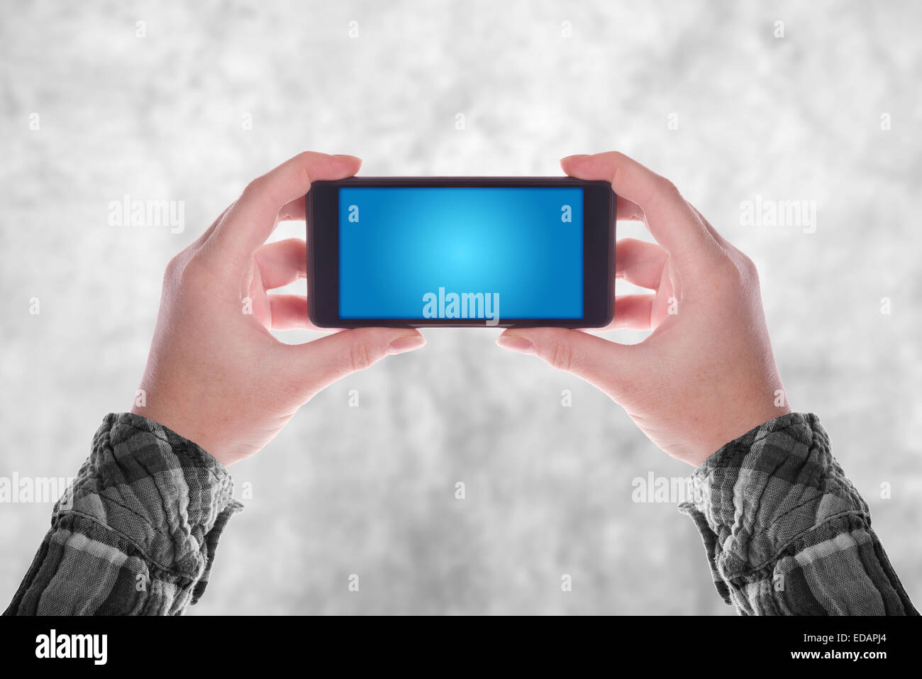Hands holding Smartphone Device in Vertical Position with Blank Blue Screen as Copy Space Stock Photo