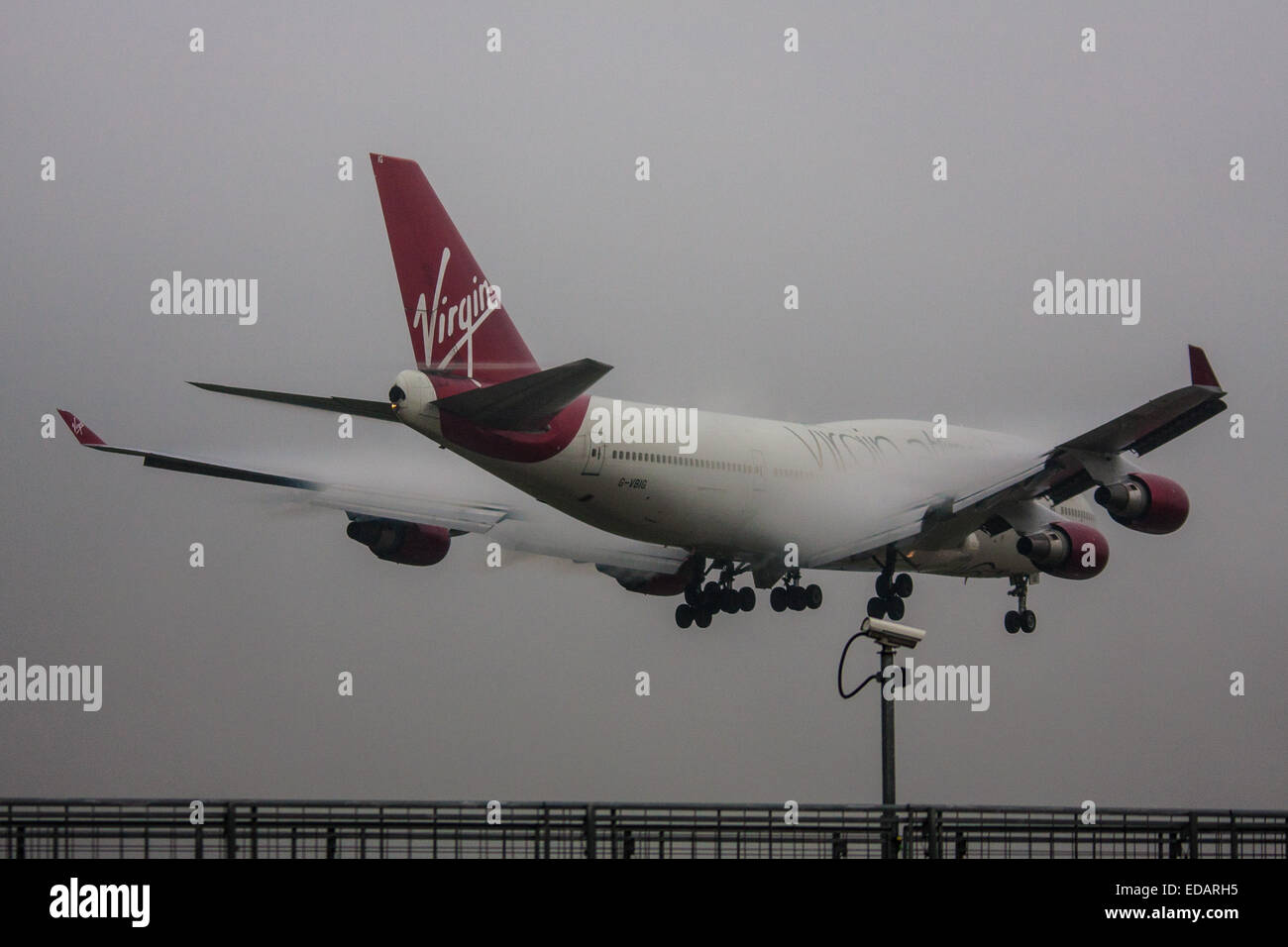 January 3rd 2015, Heathrow Airport, London. Low cloud and rain provide ideal conditions to observe wake vortexes and 'fluffing' as moisture condenses over the wings of landing aircraft. With the runway visible only at the last minute, several planes had to perform a 'go-round', abandoning their first attempts to land. PICTURED: Water vapour 'fluffing' over the wings of a Virgin Atlantic Boeing 747 as it lands on Heathrow's runway 27L Stock Photo