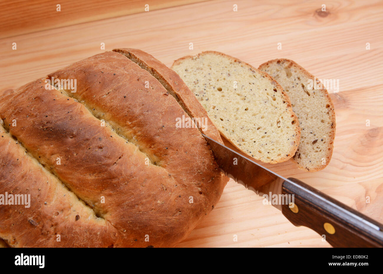 Cutting slices of bread from a freshly baked loaf on a wooden table Stock Photo