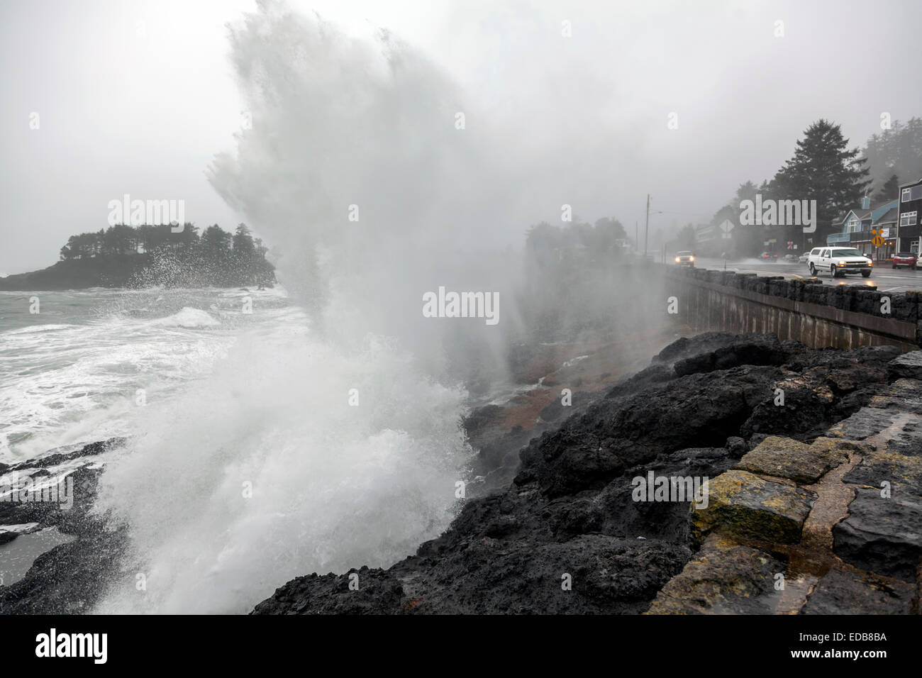 Stormy surf crashes on the rocky Pacific shoreline and seawall, washing over U.S. Route 101 and car in Depoe Bay, Oregon, USA. Stock Photo
