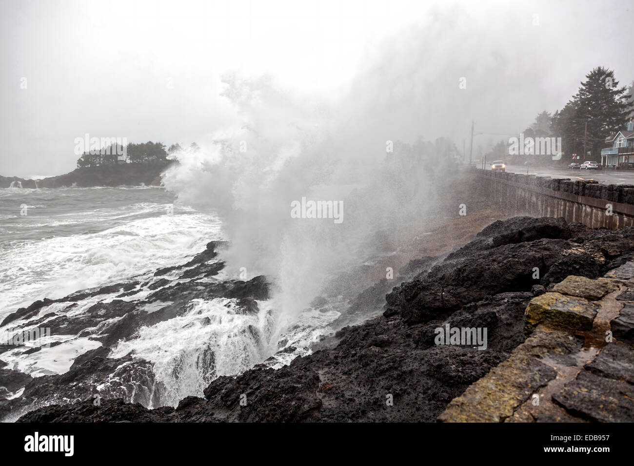 Waves crash on the rocky Pacific shoreline and seawall, washing over U.S. Route 101 and passing cars in Depoe Bay, Oregon USA. Stock Photo