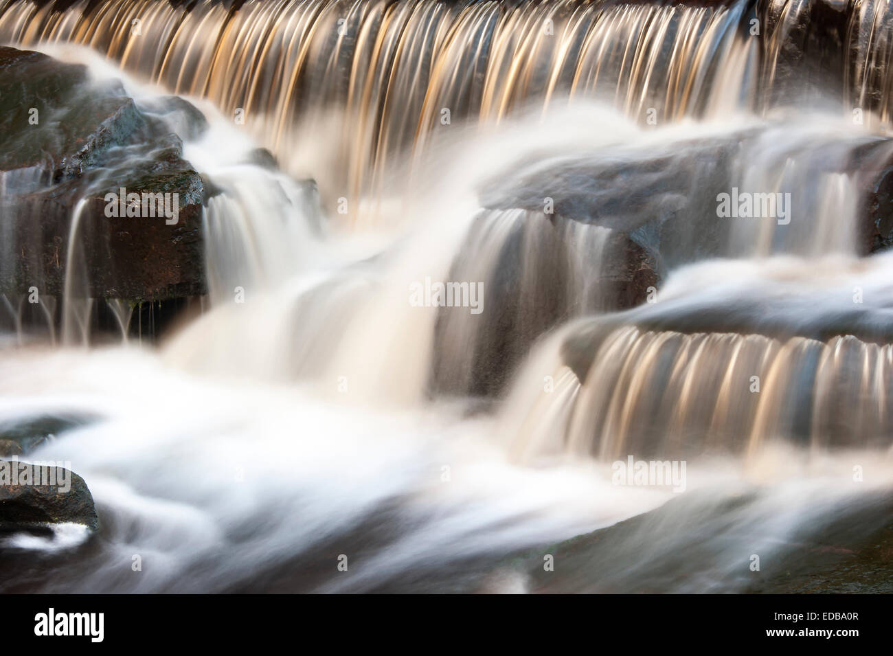 A small moorland stream cascading over a weir captured using a slow shutter speed to blur the movement of the water. Stock Photo