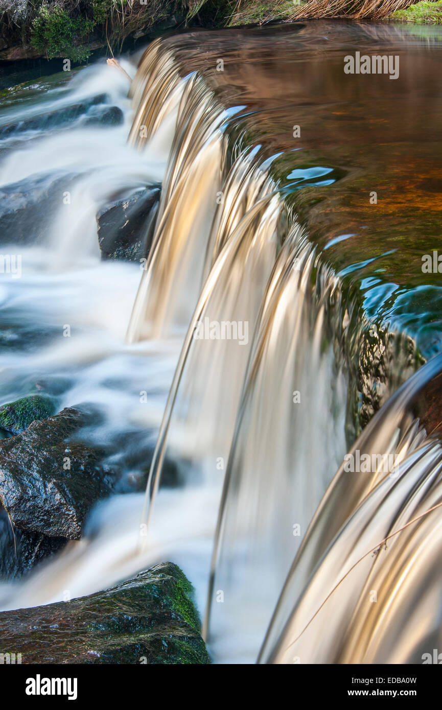 A small moorland stream cascading over a weir captured using a slow shutter speed to blur the movement of the water. Stock Photo