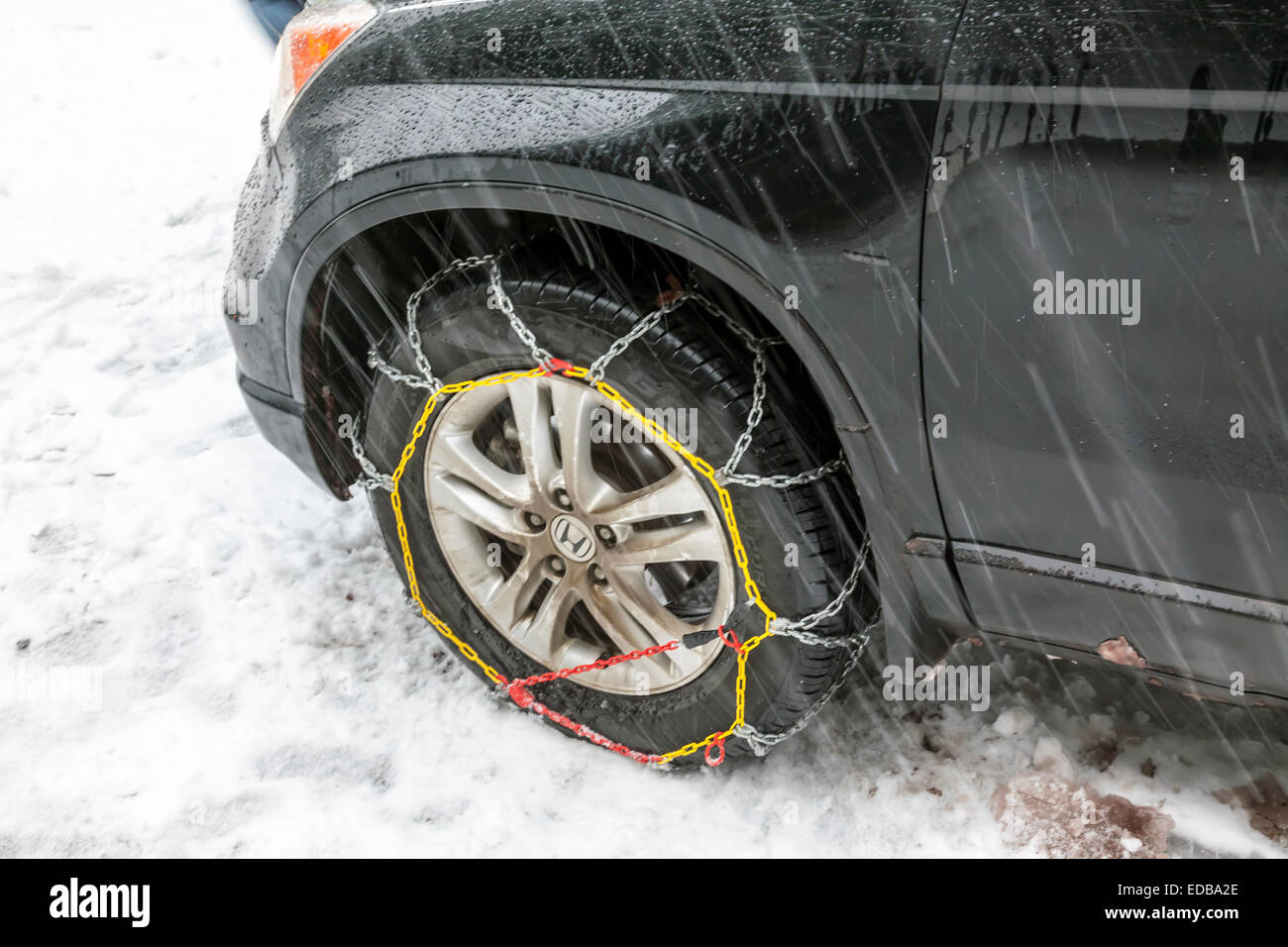 Snow chains installed on front wheel or tire of Honda passenger car on a snowy road while snowing. Stock Photo