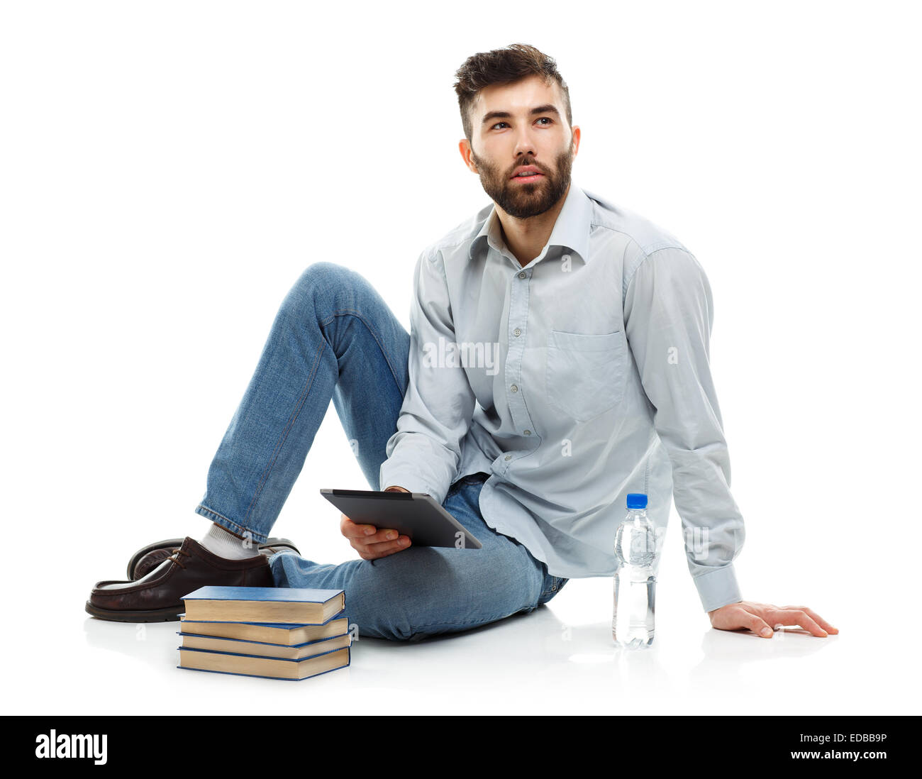Young bearded man holding a tablet with books and a bottle of water sitting on a white background Stock Photo