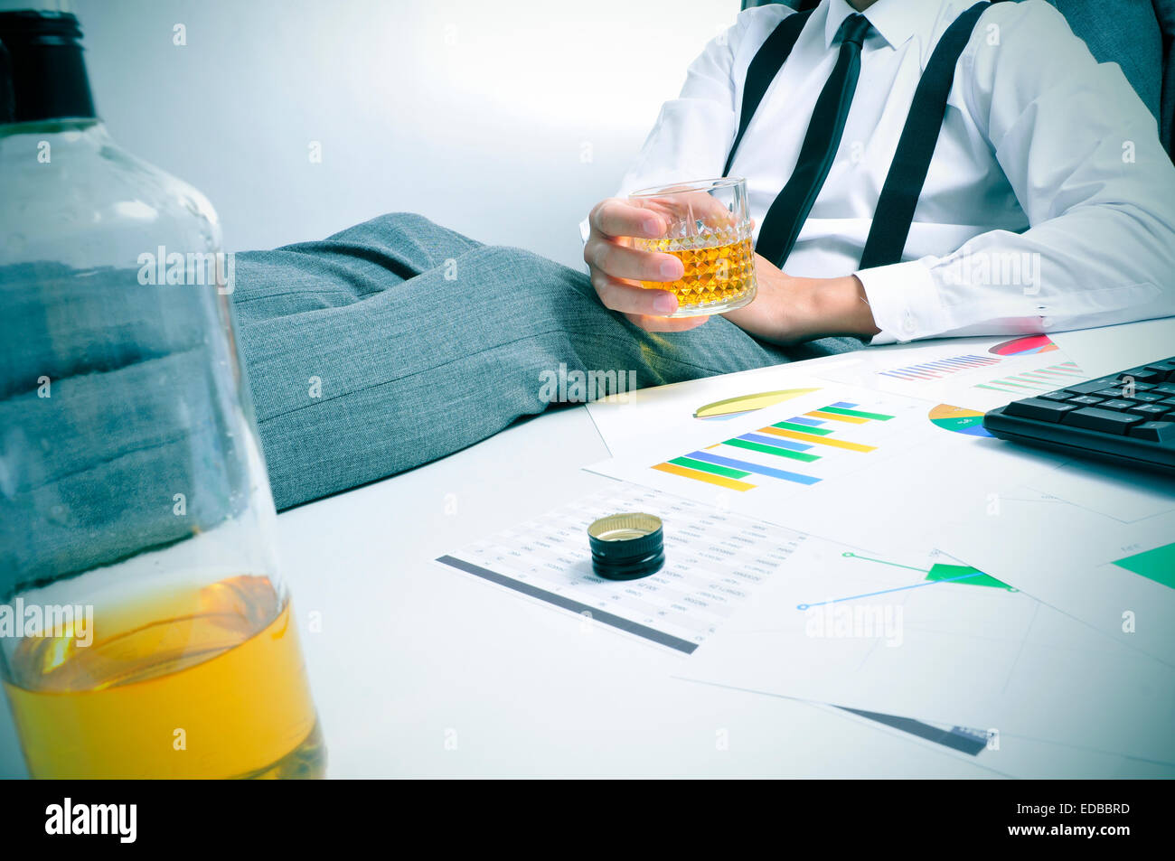 a young businessman sitting at his office desk with a glass with an alcoholic beverage in his hand Stock Photo