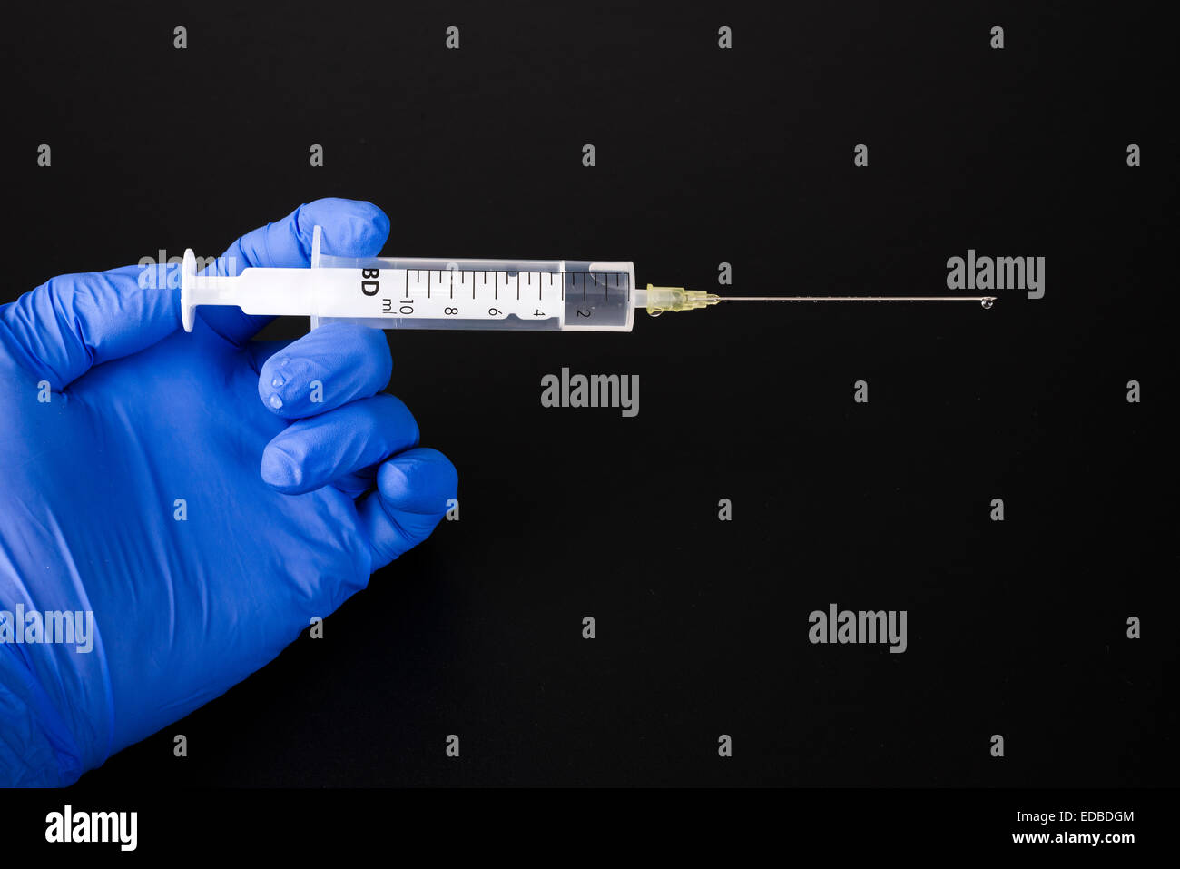A hand with a blue medical glove is holding a syringe Stock Photo