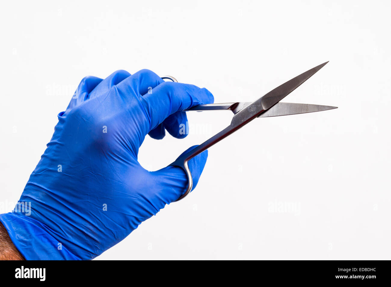 A hand with a blue medical glove is holding a pair of scissors Stock Photo