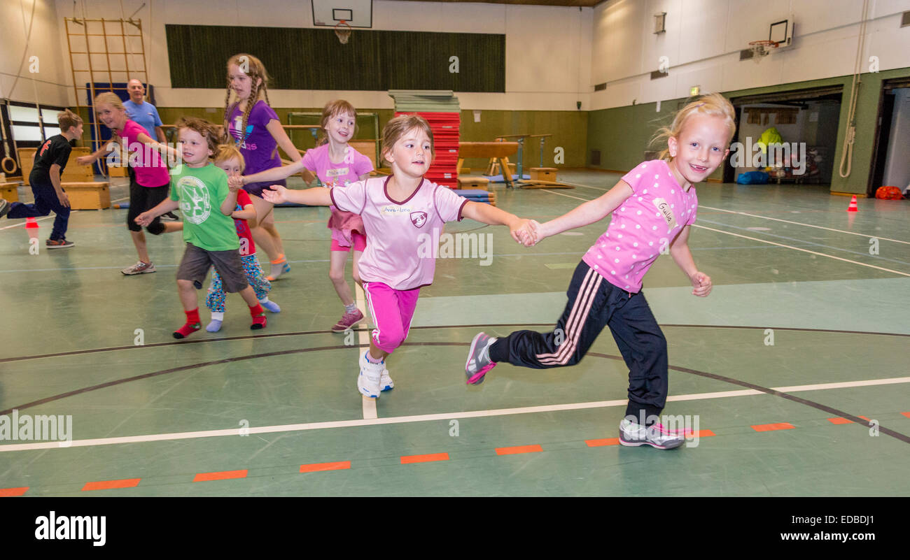 Three to eleven year old girls and boys run around in a sports hall. Stock Photo