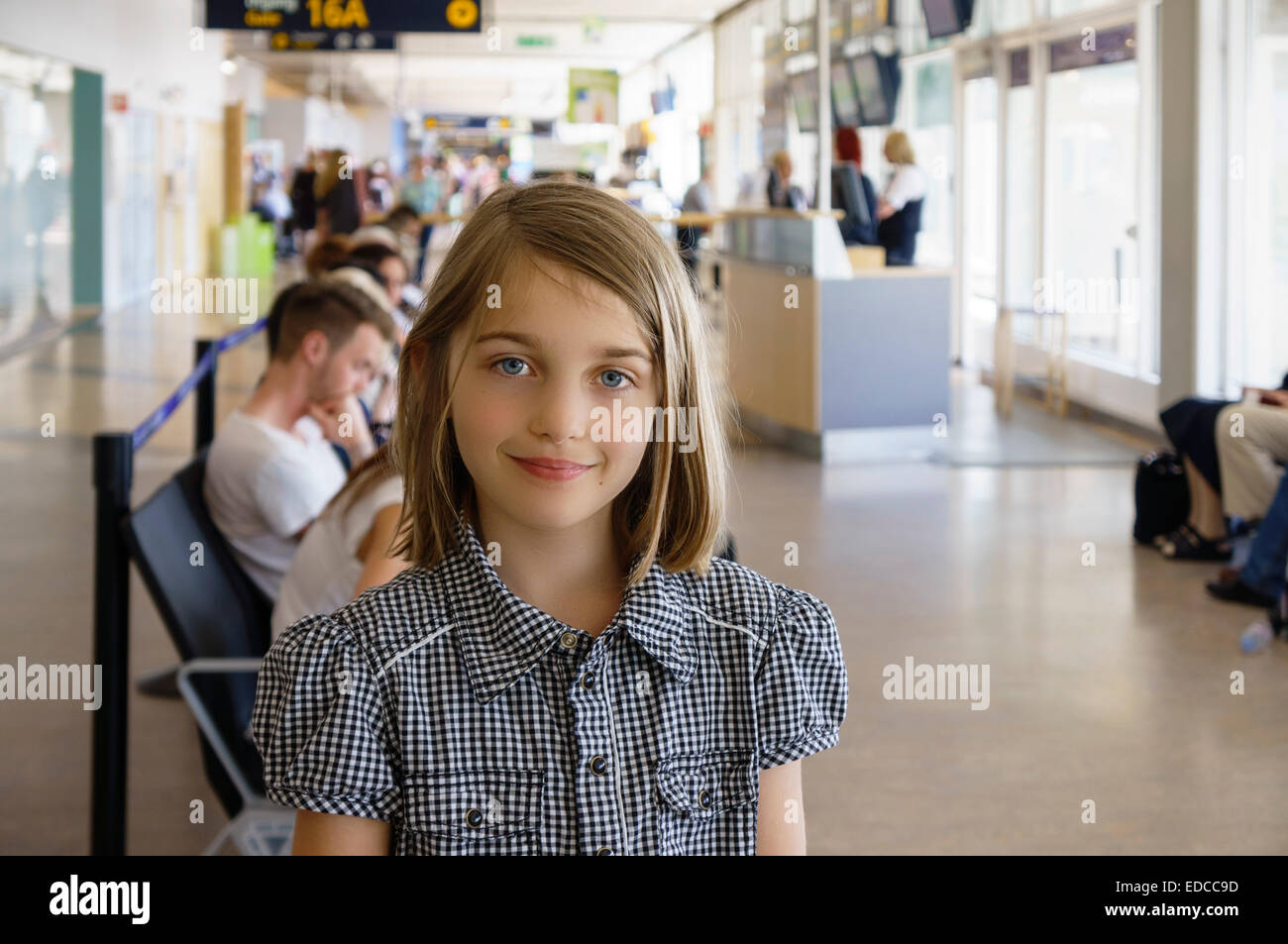 Young girl looking at camera waiting at airport boarding gate lounge  Model Release: Yes (young girl only).  Property Release: No. Stock Photo