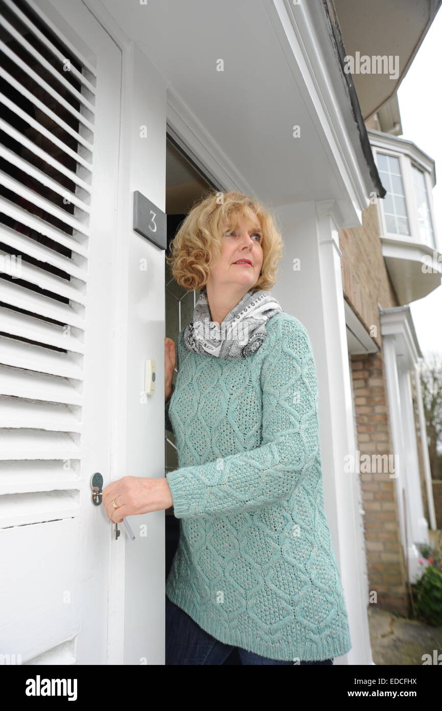 Woman looking out of her front door to greet visitors and locking bin cupboard security at home Stock Photo