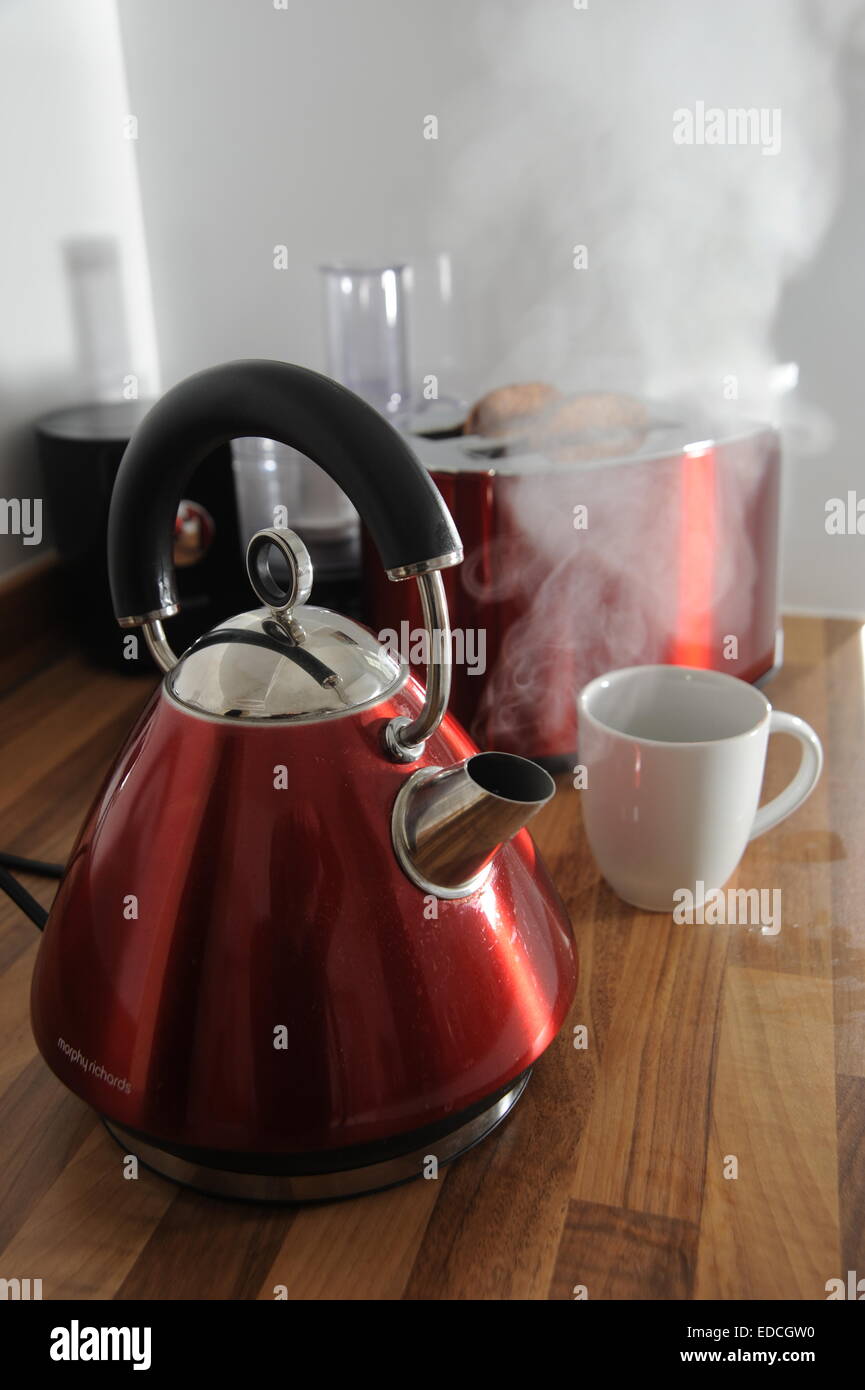 Kettle boiling with steam and toaster cooking toast behind in kitchen