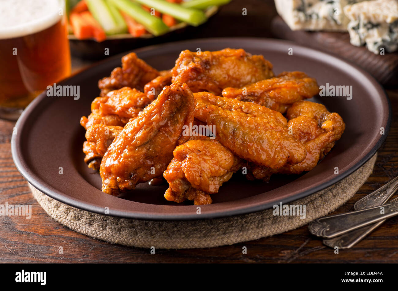 A plate of delicious buffalo style chicken wings with hot sauce, blue cheese, celery sticks, carrot sticks, and beer. Stock Photo